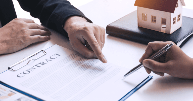 A person pointing to a document for another person to sign, with a miniature house beside them. Contact our accounting firm in Sydney for help with real estate financial planning and taxes.