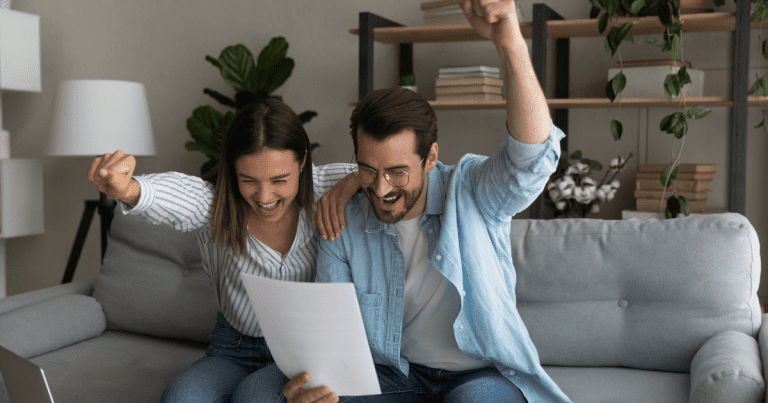 Two people are sitting on a couch in a home setting, looking at a document together with big smiles on their faces. Contact our small business accountants in Sydney for help with financial planning and tax preparation.