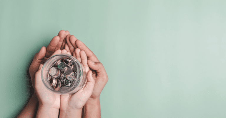 Two pairs of hands are holding a glass jar filled with coins. Get help managing your finances with our team of experienced accountants in Sydney.