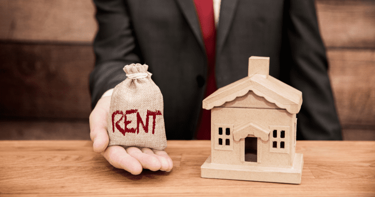 A person carrying a sack labelled with "rent" standing beside a miniature house. Contact our small business accountants in Sydney to help you manage your expenses and optimize your financial strategy.