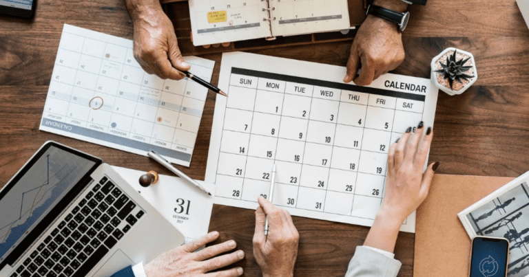A group of people gathered around a table working on a calendar, with a laptop visible. Contact our accounting firm in Sydney for help with bookkeeping and financial management, and let us help you achieve your financial goals.