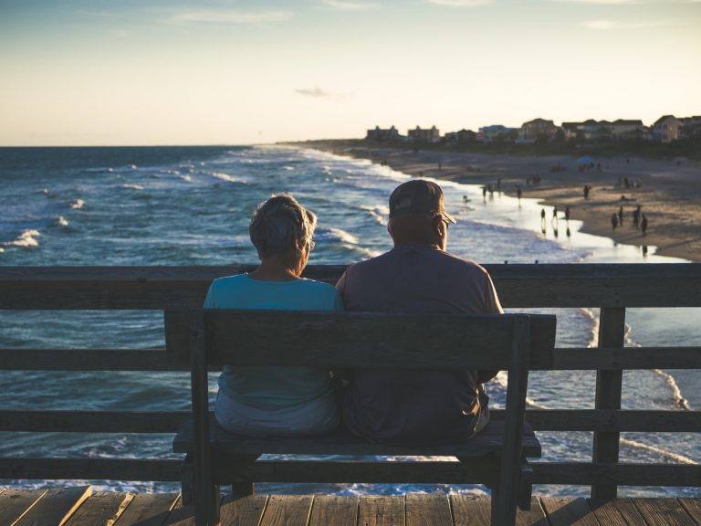an old man and woman sitting infront of the beach