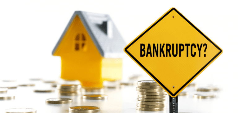Bankruptcy sign with scattered coins and a miniature house in the background. Seek the advice of a trusted tax accountant to help with financial planning and avoid financial difficulties.