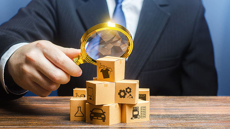 A small business accountant uses a magnifying glass to examine a pile of wooden blocks with investment and insurance icons.