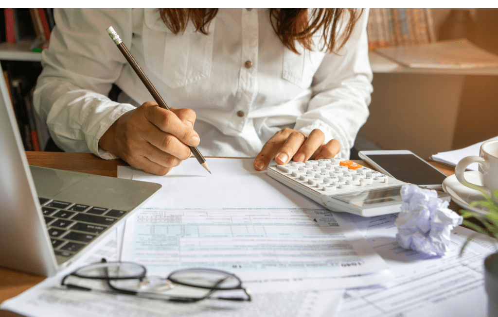 A focused woman meticulously reviewing financial statements with a pencil in hand, surrounded by a calculator and documents, illustrating  tax planning and financial management.