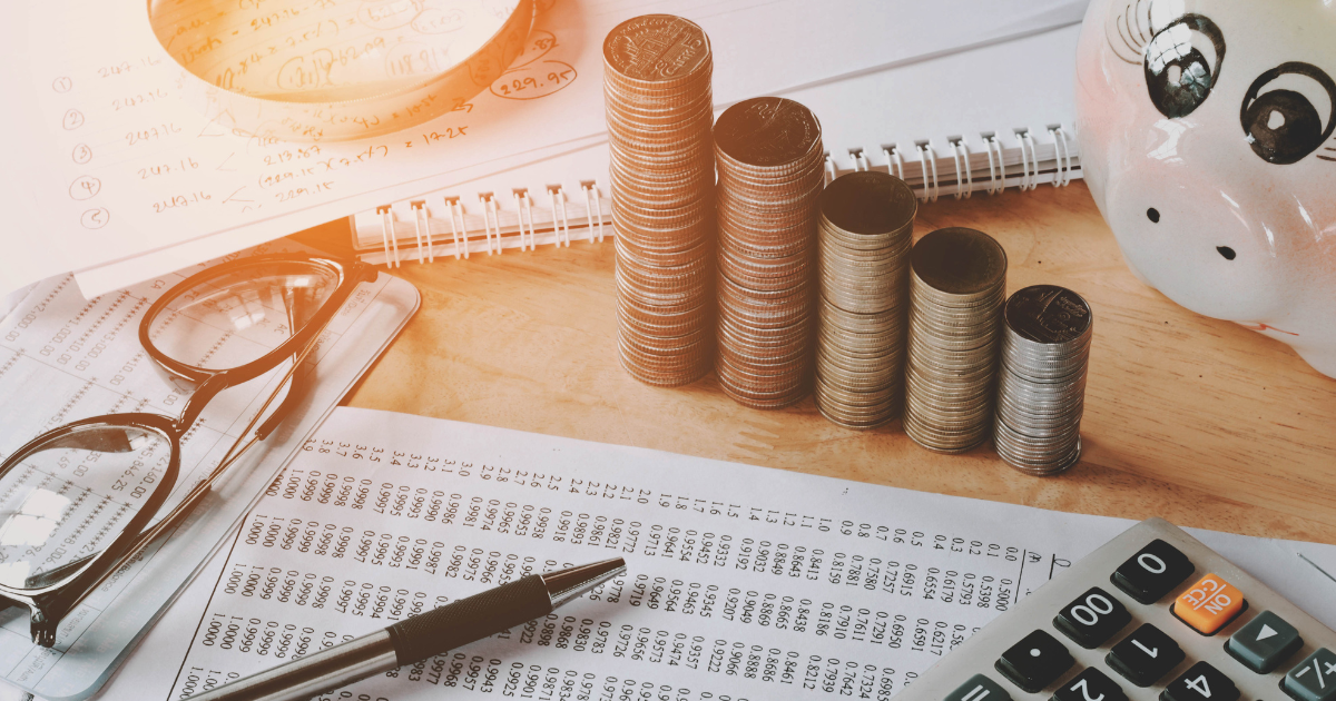 A variety of financial tools vital for business accountants during tax preparation and accounting, including coins, a pen, a calculator, a piggy bank, and financial data, laid out on a table.