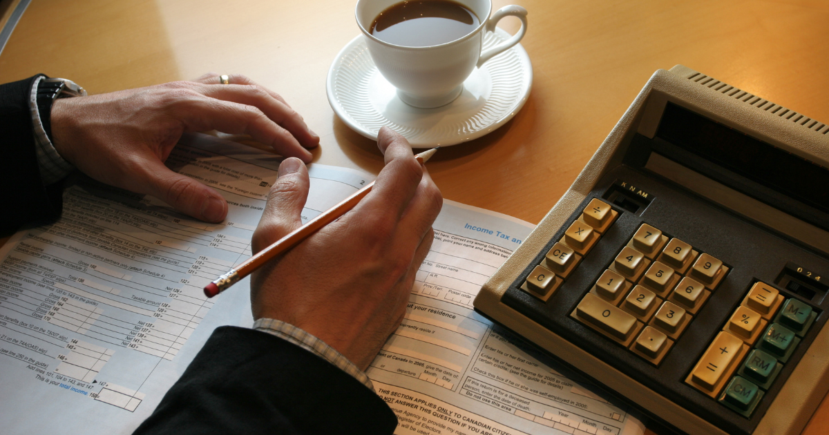 A man about to fill up an ITR form with a calculator and a cup of coffee on the table. Our tax accountants can help you prepare and file your tax returns accurately while maximising your deductions.