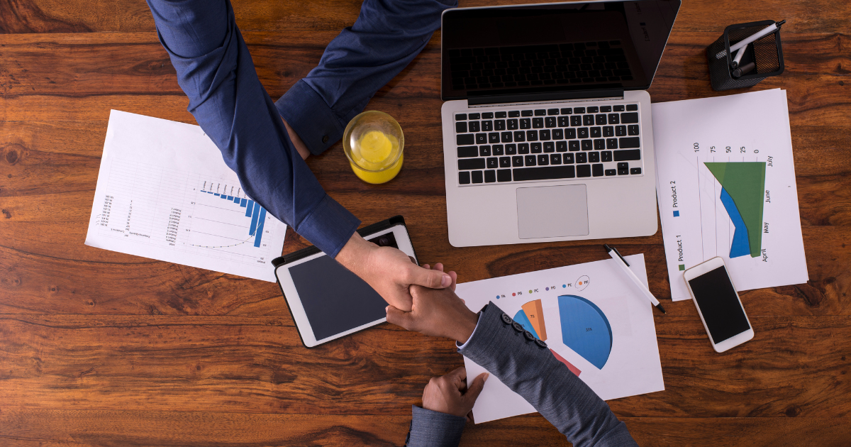 Two individuals shaking hands over a table with financial documents and electronic devices. Trust our experienced small business accountants in Sydney for reliable financial advice and guidance.
