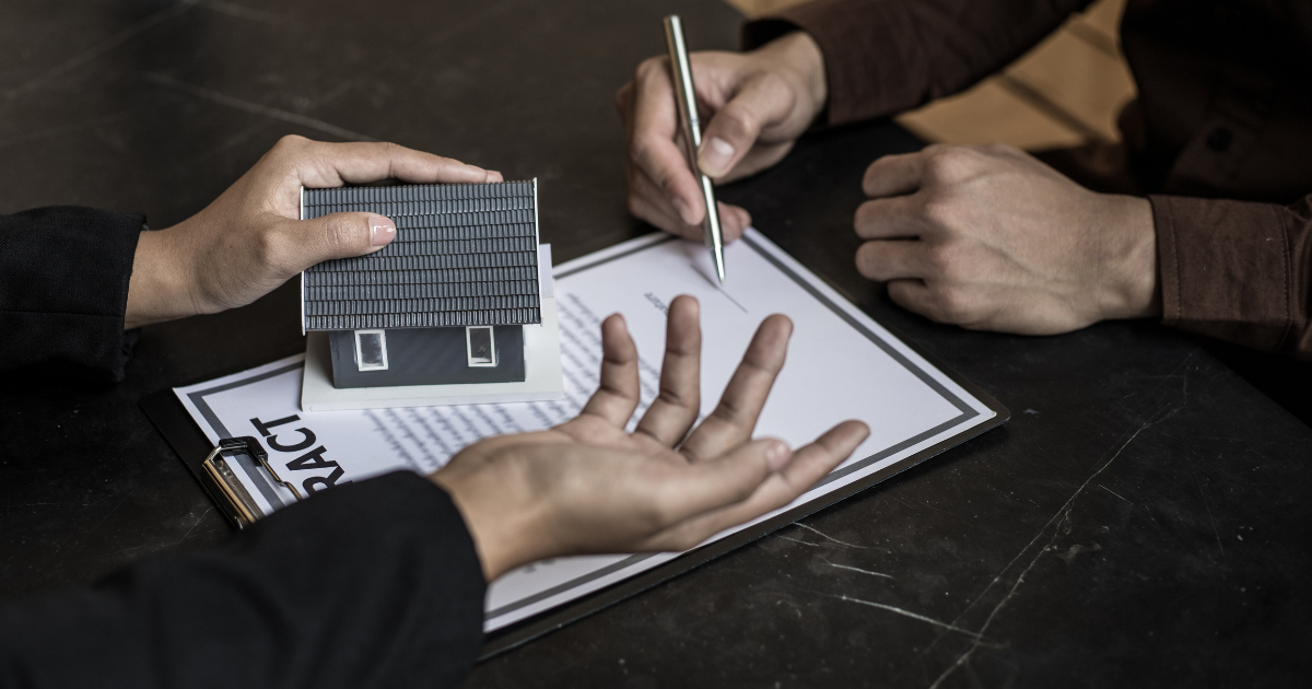 A person is being handed a miniature house while preparing to sign a contract, underscoring the value of working with a knowledgeable tax accountant near them for assistance in managing their finances.