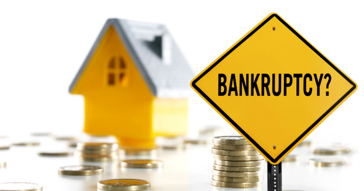 Bankruptcy sign with scattered coins and a miniature house in the background. Seek the advice of a trusted tax accountant to help with financial planning and avoid financial difficulties.