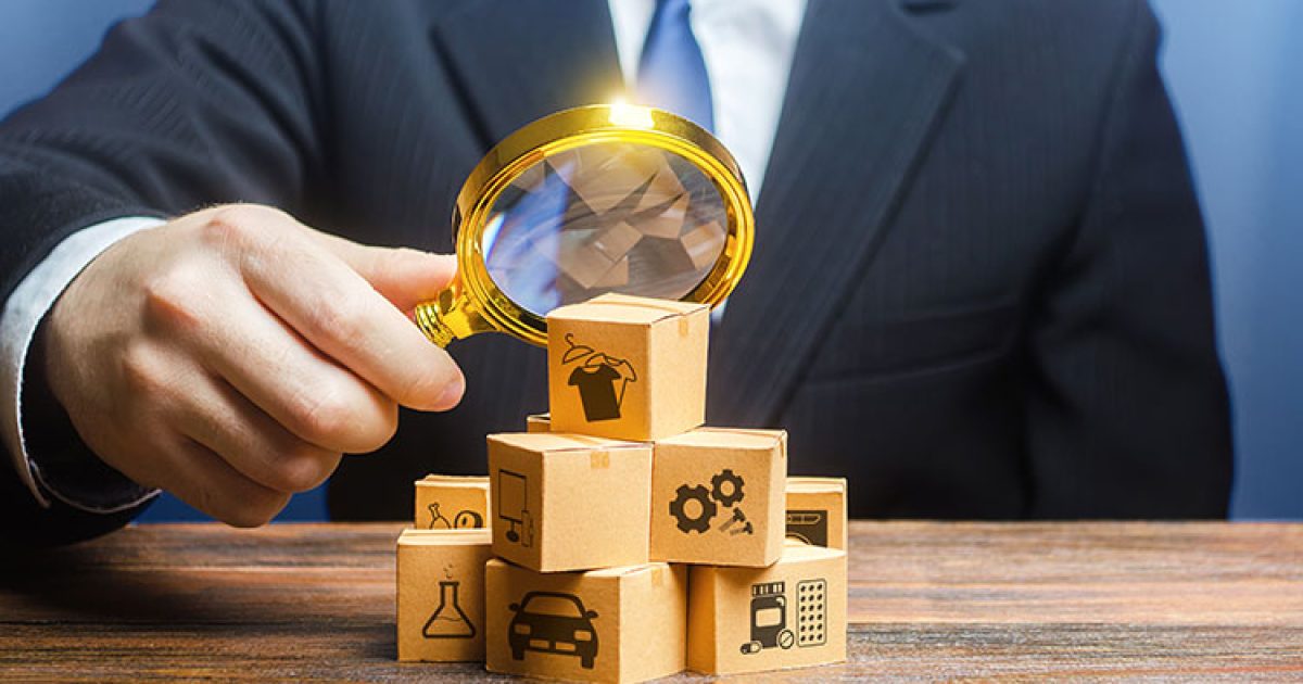 A small business accountant uses a magnifying glass to examine a pile of wooden blocks with investment and insurance icons.